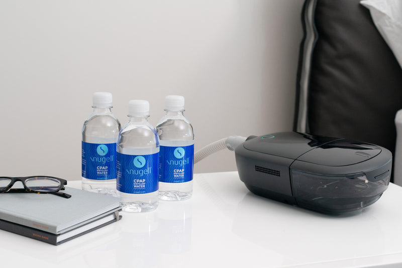 Three 12oz distilled water bottles by Snugell on a nightstand next to a CPAP machine